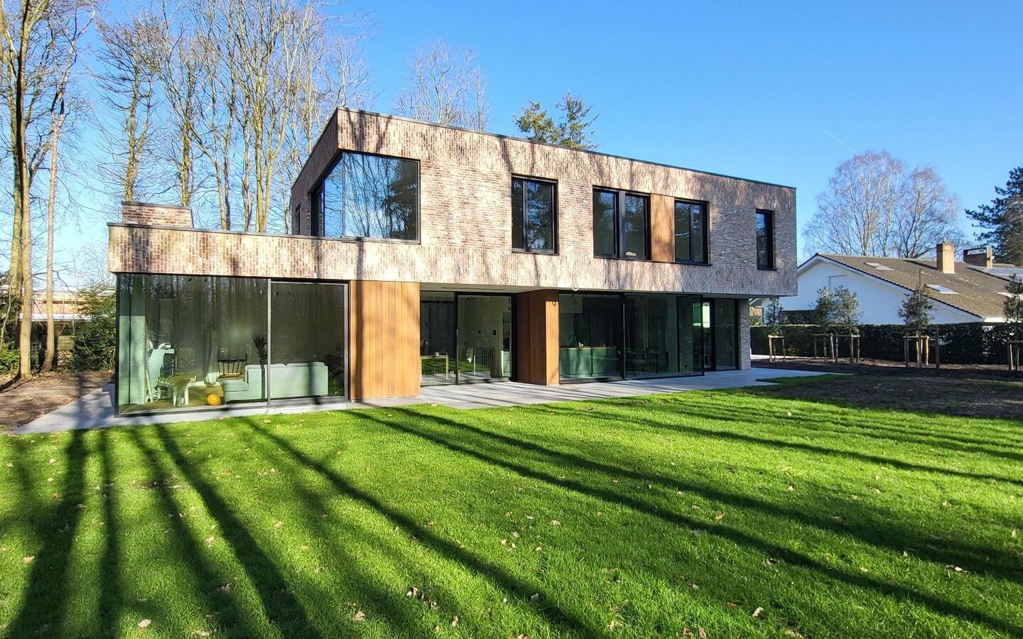 Moderne villa met zwarte aluminium ramen en natuurlijke houten gevelbekleding, omringd door bosrijk domein.